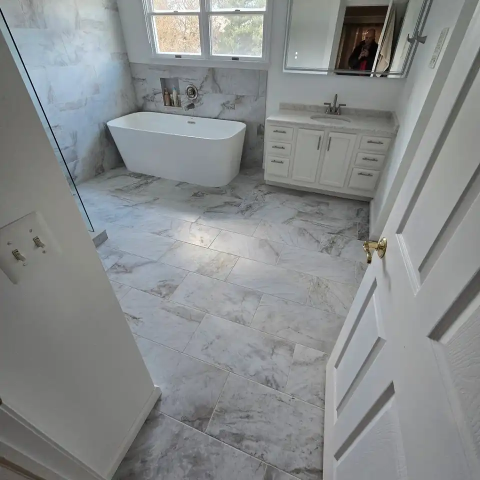Freestanding tub under a window on a marble-look floor with a white vanity