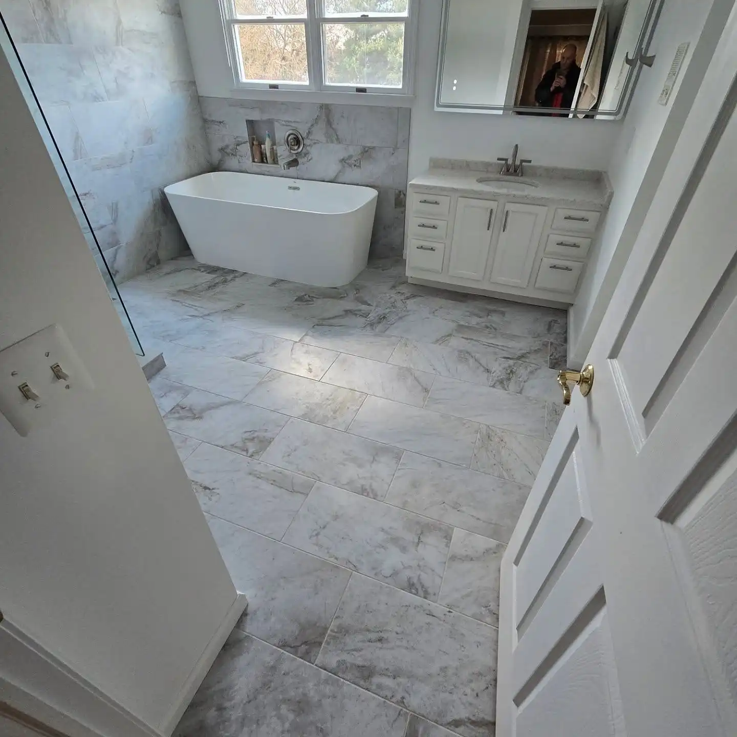 Freestanding tub under a window on a marble-look floor with a white vanity