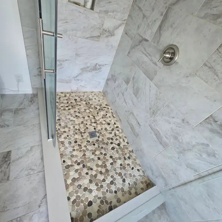 Pebble mosaic shower floor sloping to the drain, curb edge in the foreground