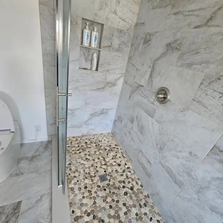 Pebble mosaic shower floor meeting the marble-look wall tile