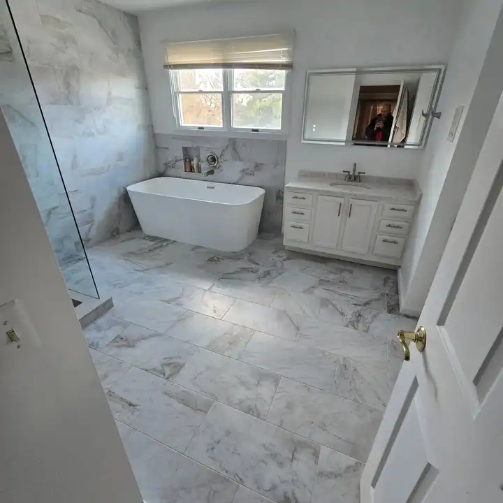 White freestanding tub beside a white vanity, window light across the marble floor