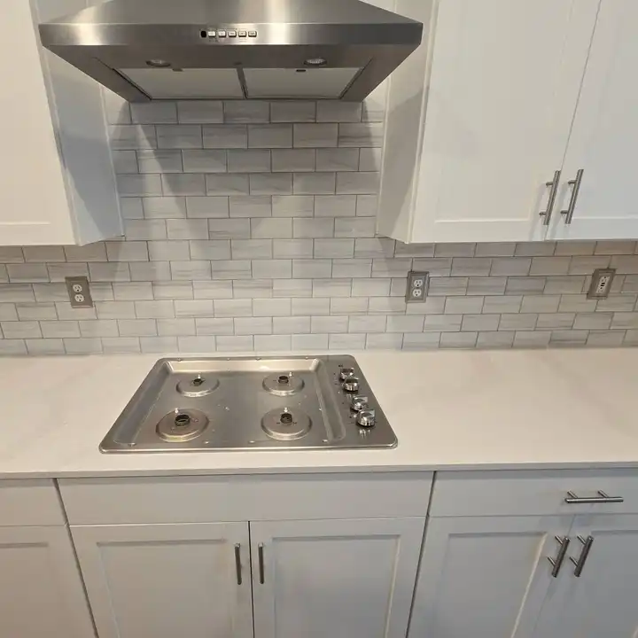 Grey subway backsplash behind a gas cooktop under a stainless range hood