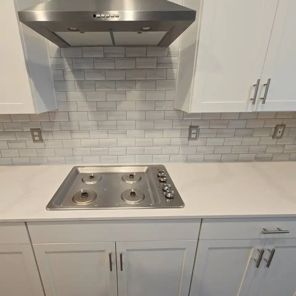 Grey subway tile backsplash behind a gas cooktop under a stainless hood