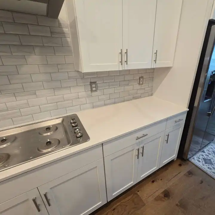 Grey subway backsplash running along white cabinets to the corner