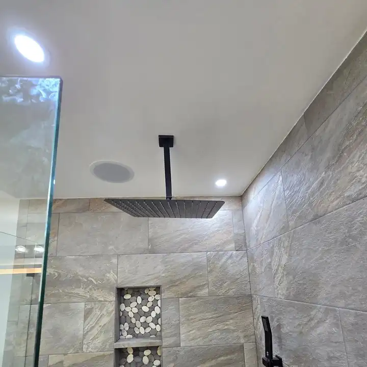 Black ceiling rain head above the stone-look shower wall