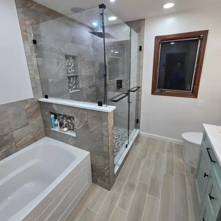Glass shower panel beside a wood-framed window, stone-look walls