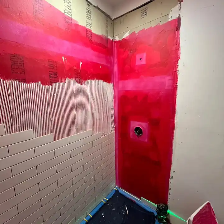 Shower walls and curb coated in red liquid waterproofing membrane before any tile