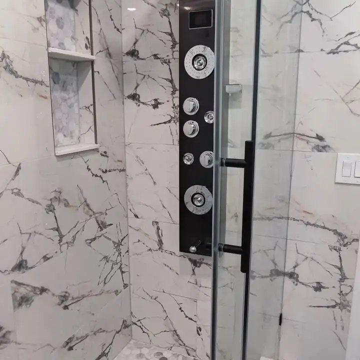 Black shower panel with body jets beside a recessed niche in marble-look tile