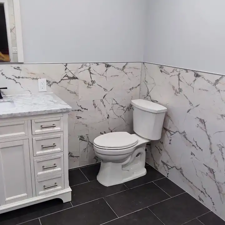 White vanity against a marble-look tile wainscot on a dark plank floor