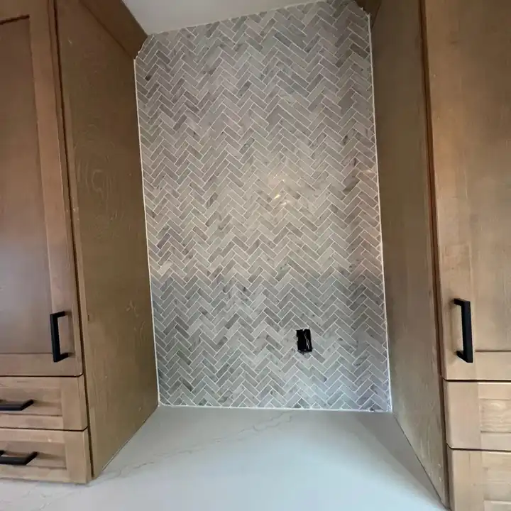 Herringbone marble backsplash running into a tall oak pantry cabinet
