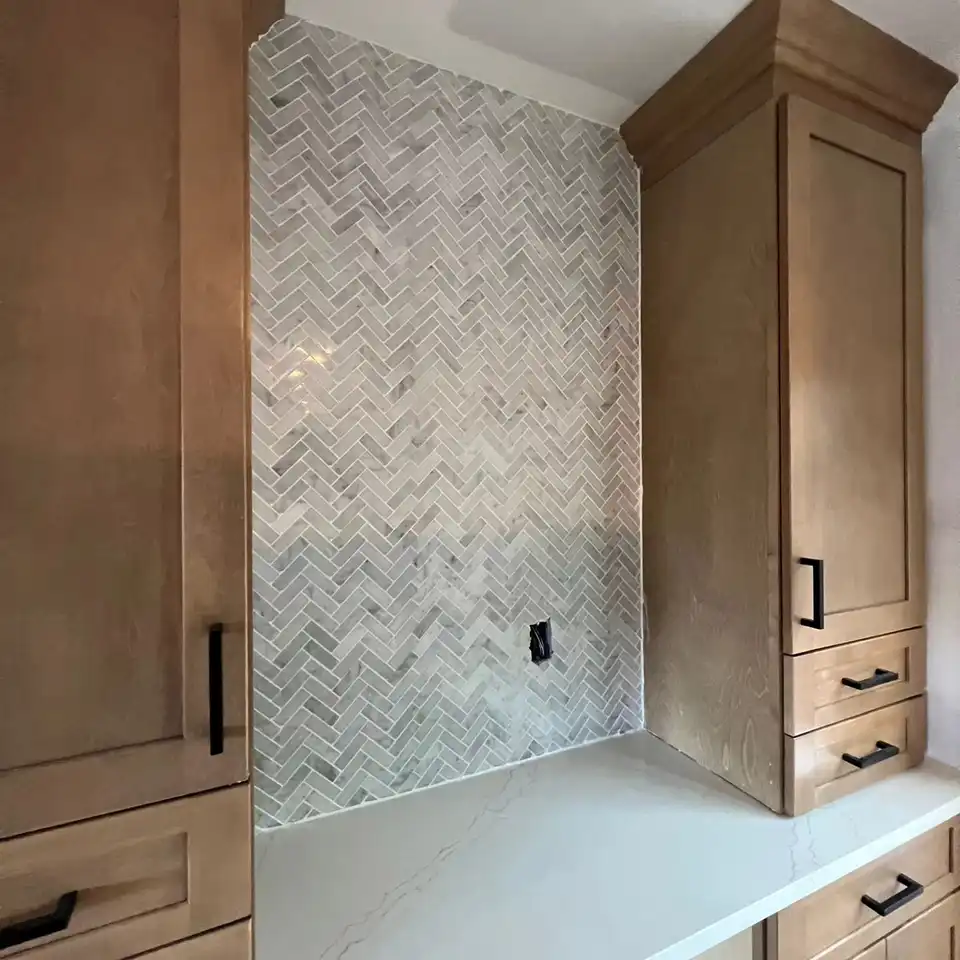 Marble herringbone backsplash between white oak cabinets and a white quartz counter