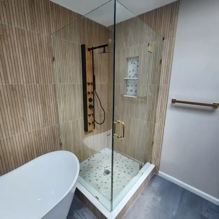 Glass corner shower with a black panel and a pebble floor, wood-look walls