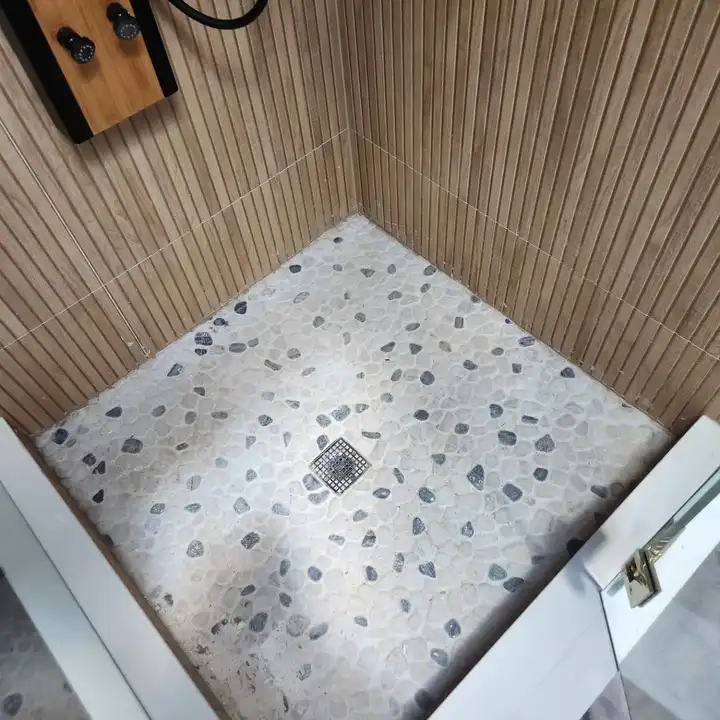 Pebble mosaic shower floor meeting the wood-look wall tile at the corner