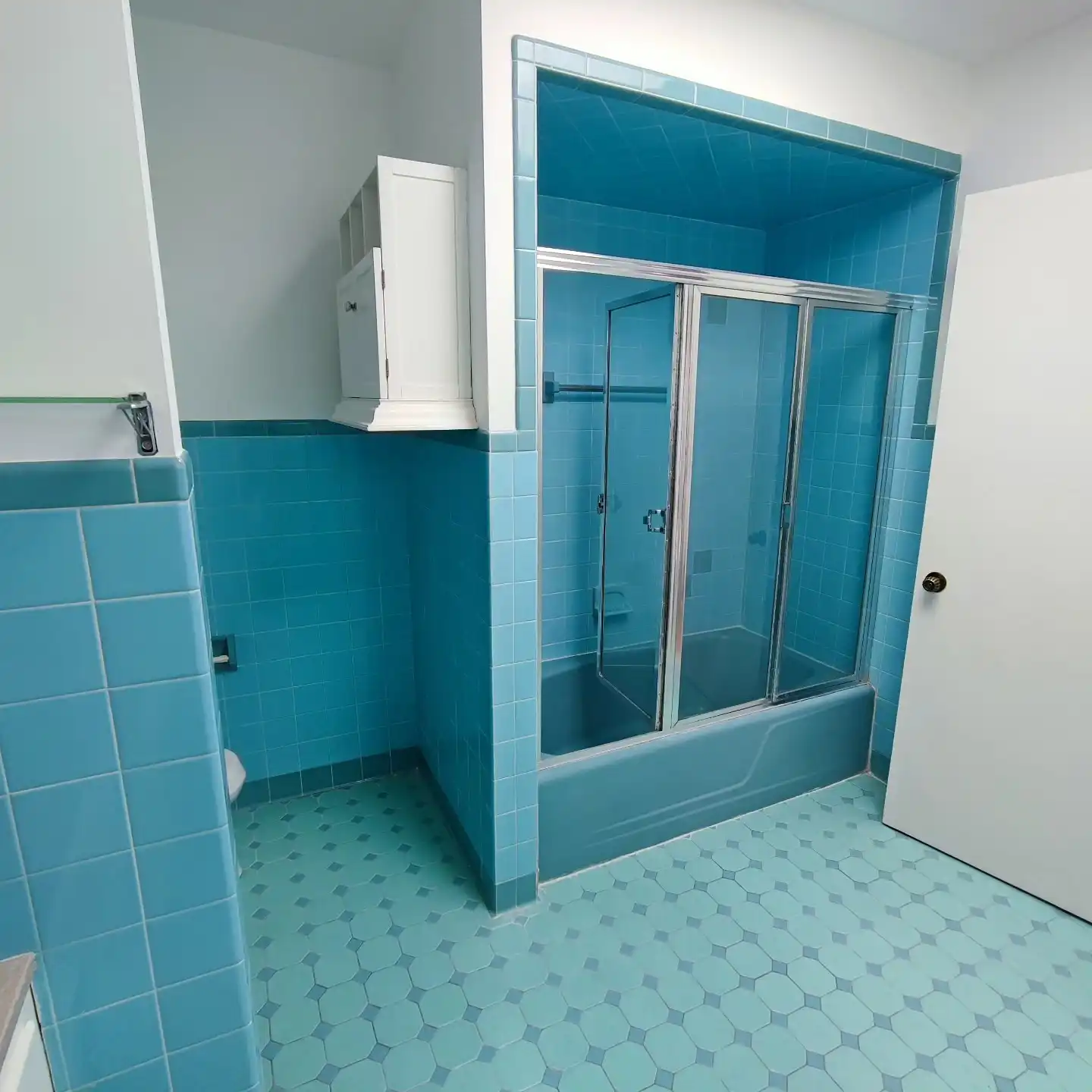 Original 1960s bathroom with turquoise wall tile, glass tub doors and a white vanity