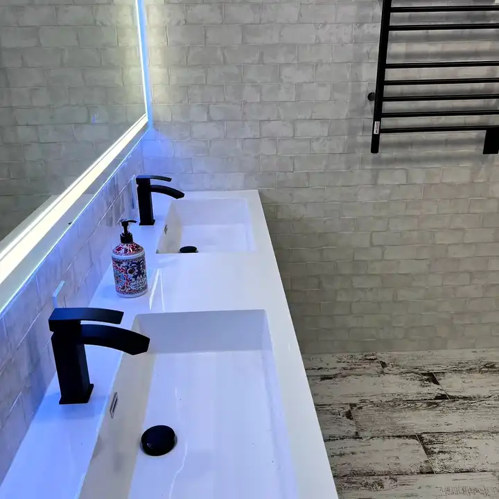 Double white sink with two wall-mounted matte black faucets on handmade-look tile
