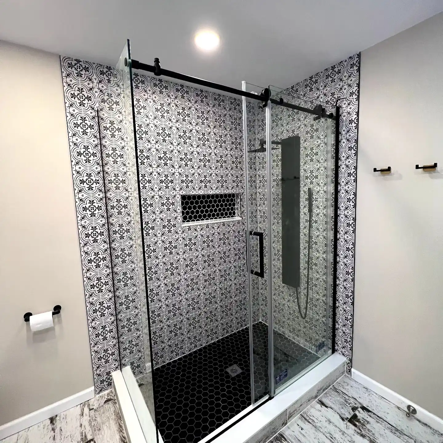 Black-framed sliding shower door in front of black and white patterned porcelain tile