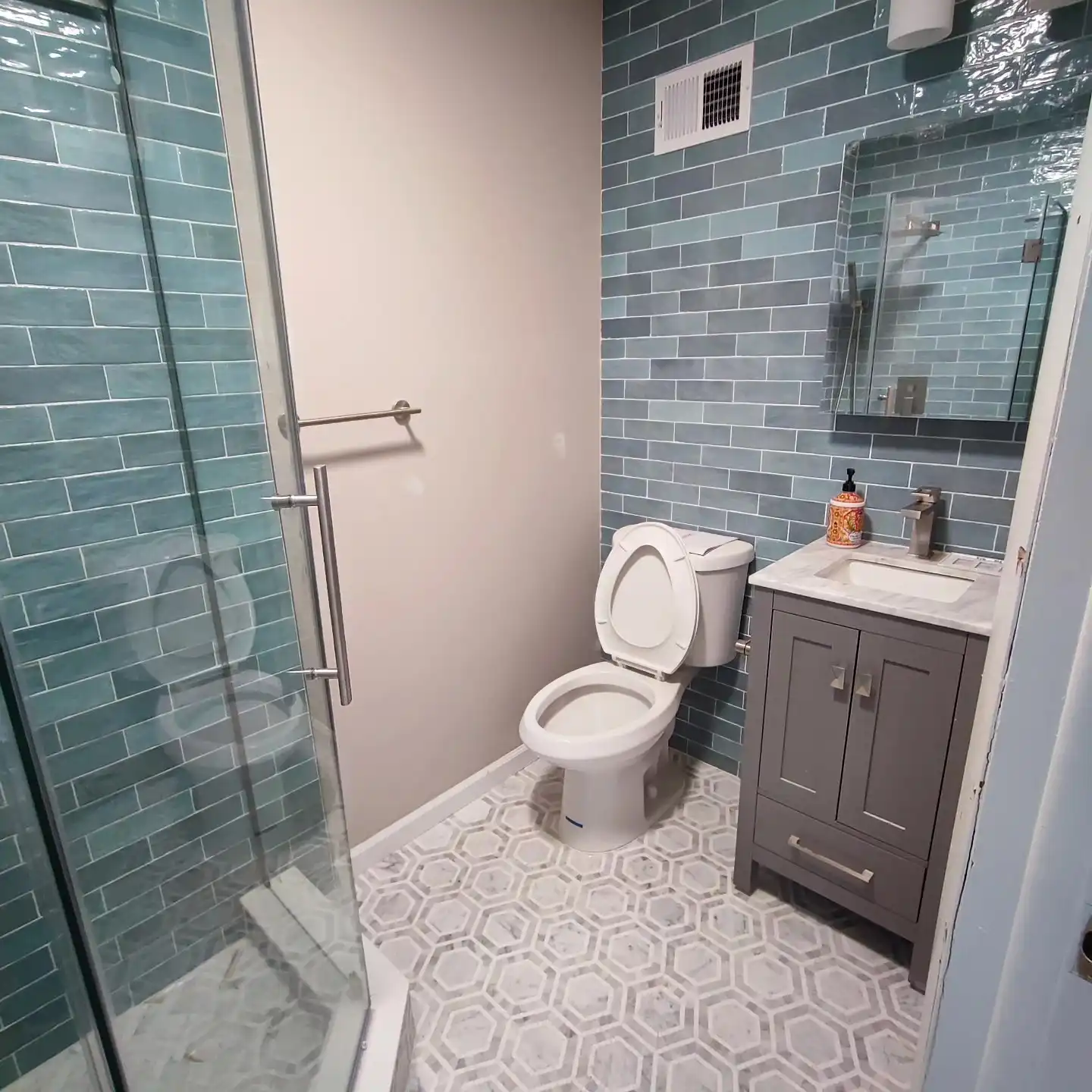 Corner shower in sea-green subway tile with frameless glass and a white hexagon floor