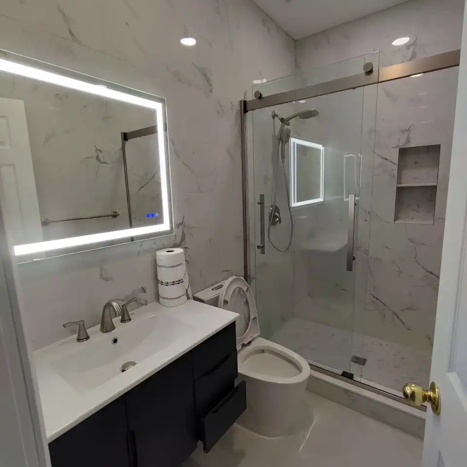 Marble-look bathroom with an LED mirror over a black vanity and a sliding glass shower