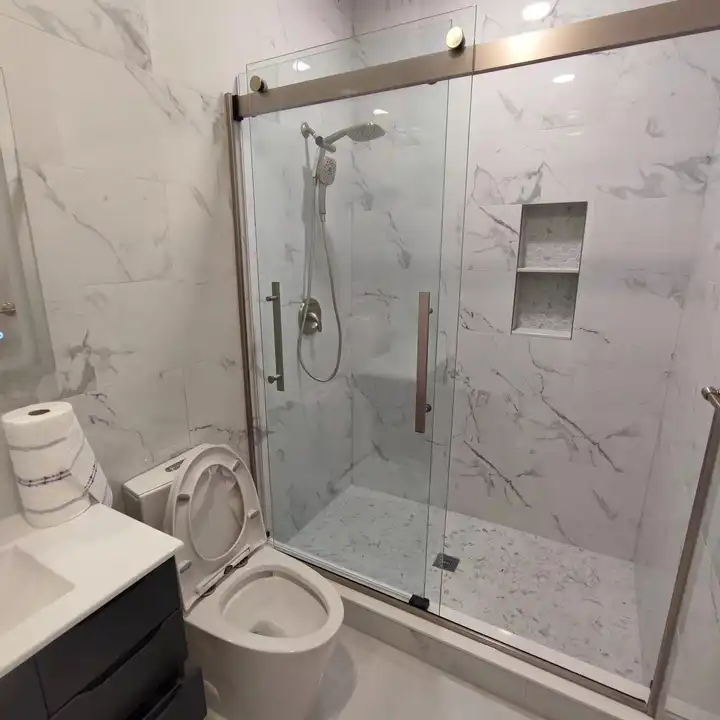 Frameless sliding shower door showing a recessed niche in the marble-look wall