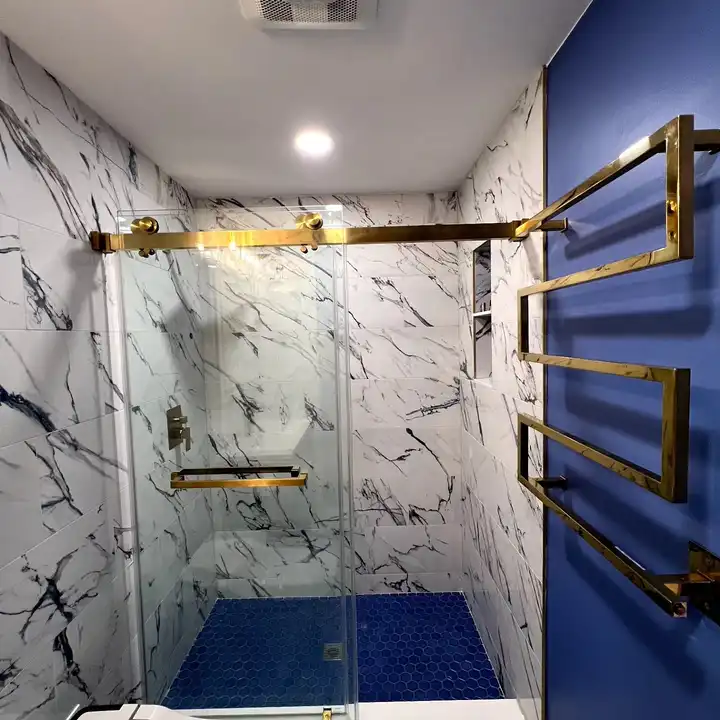 Gold-framed sliding shower door with a navy mosaic floor behind it