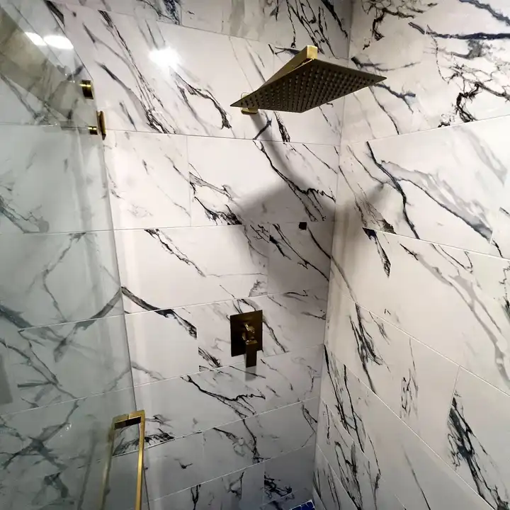 Gold rain head on a marble-look wall with the veining running through the corner