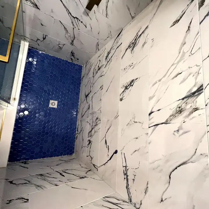 Navy glass mosaic shower floor against bold-veined marble-look walls